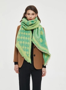 Detail of thick knitted shawl featuring green and yellow polka dots with tassel edges