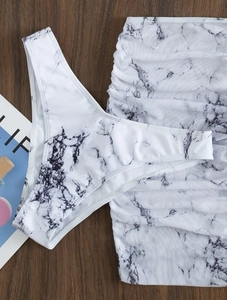 Flat lay detail of marble print bikini bottoms and mesh ruched skirt on dark wood
