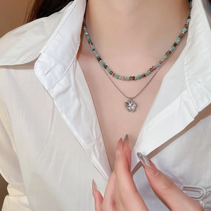 Close-up of double-layered stainless steel flower pendant and colored bead necklace