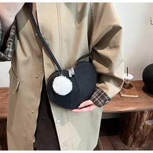 Detail der herzförmigen Umhängetasche mit weißem Pelzanhänger am khakifarbenen Trenchcoat
