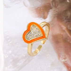 Macro detail of golden heart ring with orange enamel and micro-set white zircon stones