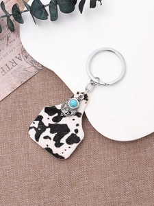 Close-up of cow print keychain charm with turquoise bead and vintage metal clasp