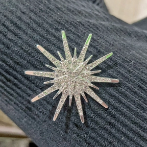 Vintage silver starburst brooch with sparkling rhinestones on black knit background