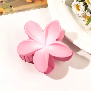 Close-up of a matte pink flower hair claw clip on a white surface with daisy decor