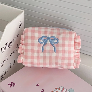 Pink checkered cosmetic bag with blue bow embroidery and ruffle edges on a desk