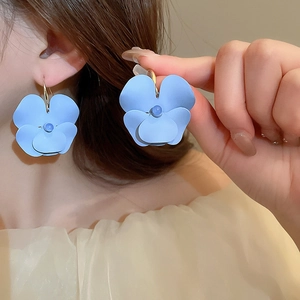Détail de boucles d'oreilles fleurs bleues mates portées pour montrer la taille