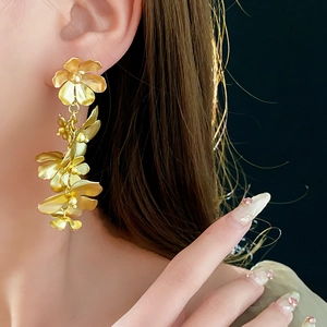 Gros plan de boucles d'oreilles fleurs dorées avec des pétales métalliques et des feuilles