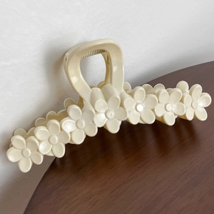 Detailed side view of a large cream floral hair claw clip on a minimalist wooden surface