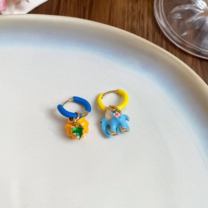 Close-up of enamel flower and elephant earrings on a white plate with a wooden background