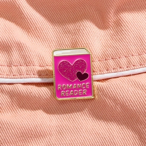 Close-up of pink glitter heart enamel pin with Romance Reader text on pink fabric