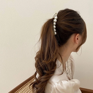 Detailed view of large gold pearl banana clip styled on model with brunette wavy hair