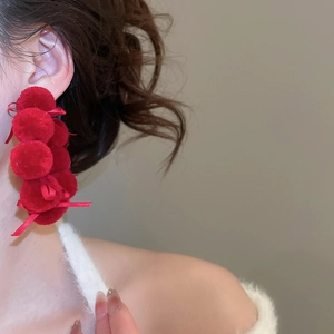 Detail of red plush pompom earrings with elegant bows for a festive autumn look