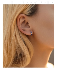Close-up of small blue heart enamel hoop earrings worn by a model in soft lighting