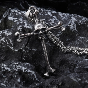 Gothic skull cross necklace in silver finish resting on dark volcanic rock background
