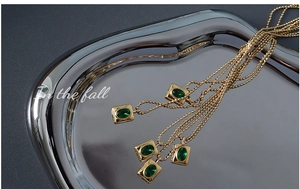 Close-up of a 18K gold-plated beaded necklace with a square green zircon pendant on tray