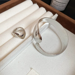 Detailed view of silver oval cuff bracelet and ring set in a minimalist luxury scene
