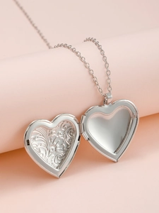 Detail view of an open silver heart locket pendant with intricate floral engravings