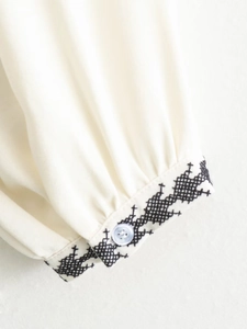 Detailed close-up of cream blouse cuff with black embroidery and single white button