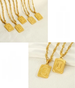 Detail of relief-engraved initial square pendants on golden stainless steel rope chains