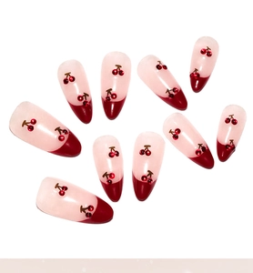 Detail of almond-shaped press-on nails with red French tips and 3D cherry rhinestone design