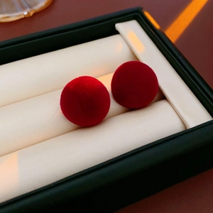 Close-up of red velvet round stud earrings in a luxury jewelry box with beige lining