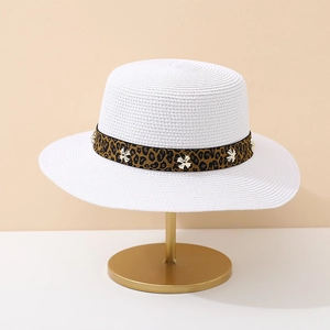 Detail of white straw sun hat with leopard print ribbon and gold metal flower accents
