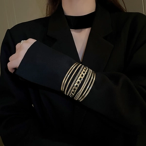 Macro detail of layered gold geometric cuff bracelet worn over a black blazer sleeve