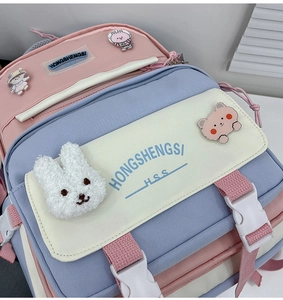 Close-up of a pink and blue canvas backpack with cute cartoon pins and a plush bunny charm