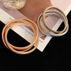 Detail of wide elastic layered snake-bone bracelets in gold and silver metallic finishes