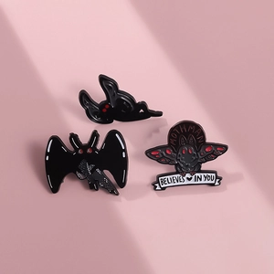 Three-piece gothic Mothman enamel pin set with red eyes on light pink background