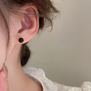 Close-up of minimalist black bead stud earring with polished finish worn on ear