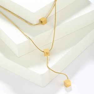 Minimalist gold snake chain necklace with three cube pendants on white geometric steps