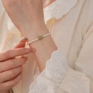 Detail of faux Hetian jade and white pearl bracelet with gold beads on wrist