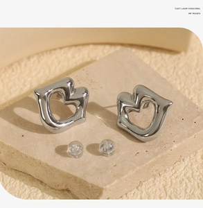 Close-up of abstract hollow heart-shaped silver stud earrings on a beige stone slab