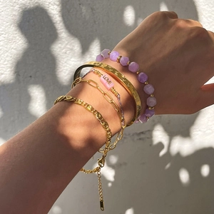 Detail of layered gold bracelets with amethyst beads and LOVE charm on a female wrist