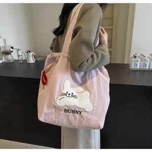 Close-up of pink tote bag with fuzzy bunny embroidery worn by a model in a cafe