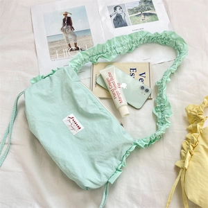 Detailed view of mint green pleated canvas crossbody bag with Zakka label on white fabric