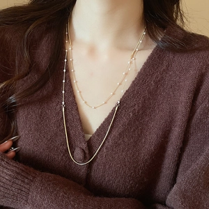 Detail of layered gold snake chain necklace with pearl accents on a V-neck cardigan