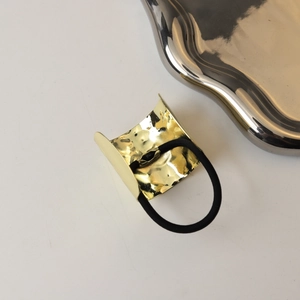 Detail of gold hammered metal hair tie with black elastic band on white background