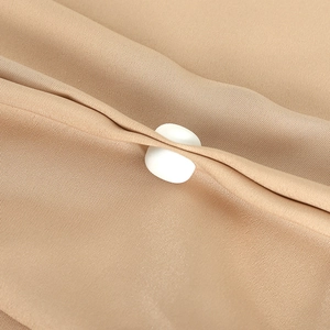 Detailed macro view of a white round fastener secured on light brown textured fabric