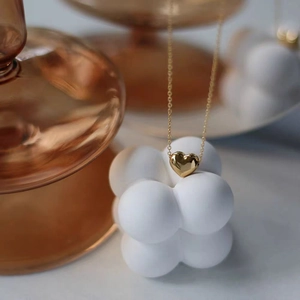 Polished 18K gold heart pendant necklace on minimalist geometric white display stand
