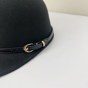 Détail d'une casquette en laine noire avec lanière en cuir et boucle métallique dorée