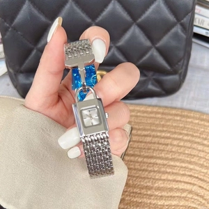 Close-up of a silver padlock-shaped watch with mesh strap worn on a wrist with a bag