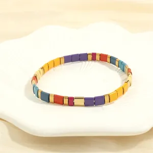 Detail of colorful enamel tile Tila bracelet with gold accents on a white shell tray