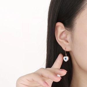 Close-up of heart-shaped evil eye earrings with gold hooks worn by a model