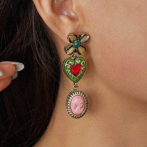 Close-up of vintage gold earrings with green clover, red heart, and pink cameo on a model