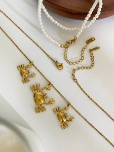 Detailed close-up of golden crab pendant on layered pearl and stainless steel necklace