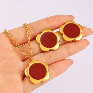 Detail view of gold flower necklace and earrings set with dark red core held in hand