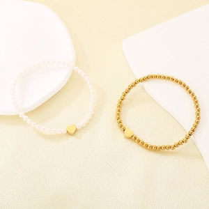 Detail of gold beaded and pearl bracelets featuring minimalist heart charms on display.