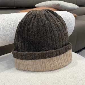 Close-up of thick rib knit texture and beige cable stitch on dark brown wool blend hat